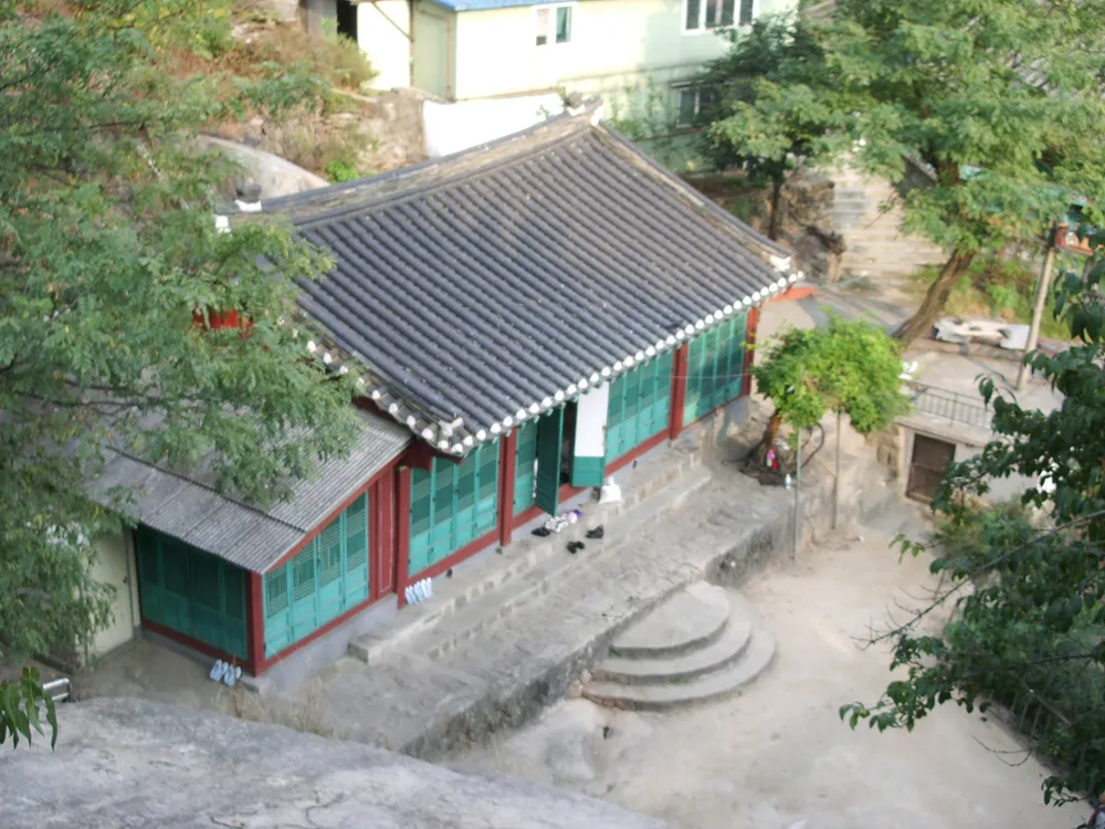 The tiled roof and painted timber front of Guksadang on the wooded slope of Inwangsan.