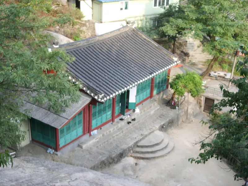 The tiled roof and painted timber front of Guksadang on the wooded slope of Inwangsan.